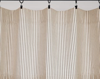 Puede incluir: Una cortina corta con un patrón de rayas verticales en beige y blanco. La tela está suspendida de una barra de metal negro mediante anillos circulares negros con clips, creando pliegues suaves y uniformes a lo ancho.