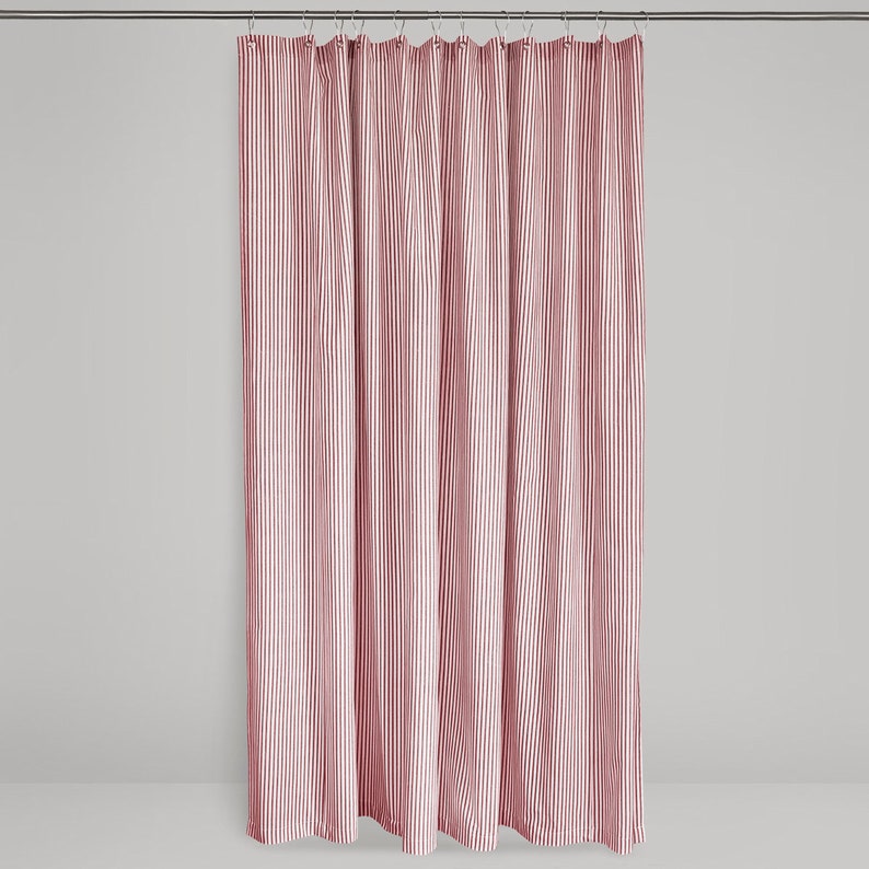 image of a red fabric shower curtain in red and cream ticking stripe fabric hanging on a shower curtain rod against a neutral background