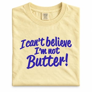 May include: A pale yellow short-sleeve t-shirt featuring the blue text "I can't believe I'm not Butter!" printed in a bold, cursive font across the chest. The shirt includes a Comfort Colors brand label at the inner neckline with size S-CH.