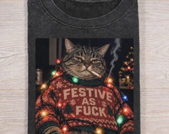 Puede incluir: Una camiseta gris carbón con el gráfico de un gato atigrado que lleva un suéter navideño rojo con el texto FESTIVE AS FUCK. El gato está envuelto en luces de colores y tiene un cigarrillo encendido en la boca con humo saliendo.