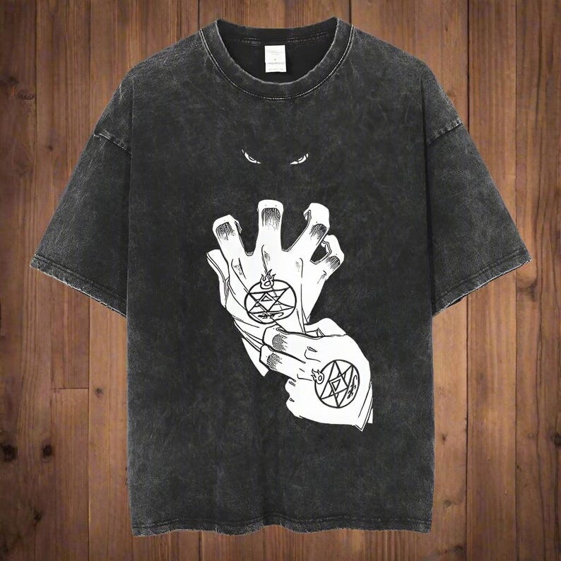 May include: Dark gray t-shirt featuring a white graphic of two hands with alchemic symbols and a pair of eyes above. The shirt has a crew neck and short sleeves. The fabric has a washed, vintage look.