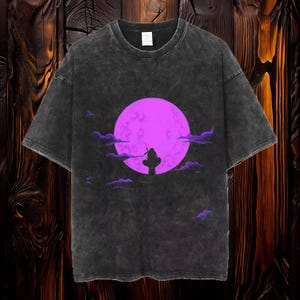 May include: A black t-shirt with a faded look features a silhouette of a person standing in front of a large, bright purple moon. The moon is surrounded by clouds.