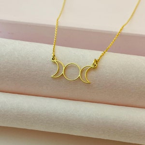 May include: A gold necklace with a triple moon pendant. The pendant is a simple design with three crescent moons.