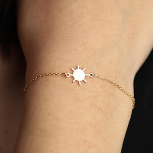 May include: A delicate gold-colored bracelet featuring a sunburst charm. The bracelet is made of a fine chain and is worn on a wrist. The sunburst charm is centered on the chain and has a detailed design.