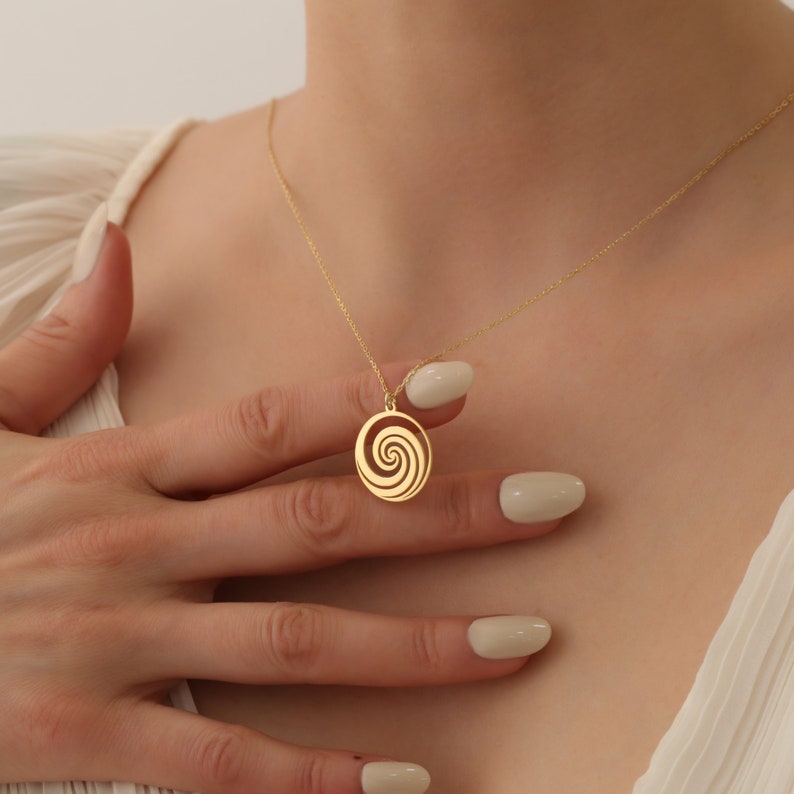 Puede incluir: Un collar de oro con un colgante circular con un dise&ntilde;o en espiral.
