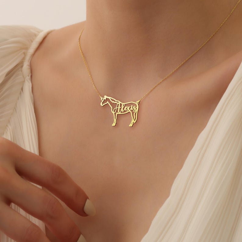 May include: Gold necklace with a horse silhouette pendant. The horse's body is cut out to spell the name "Alexis".