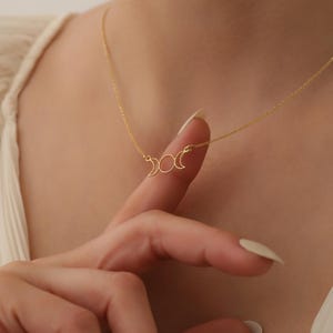 May include: A gold necklace with a delicate crescent moon pendant. The pendant features three moons in different phases, symbolising the cycle of the moon.