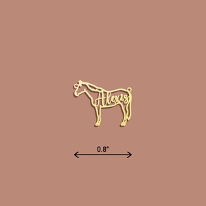 May include: Gold-colored metal horse silhouette ornament with the name "Alexis" cut out inside. The ornament is 0.8 inches wide.