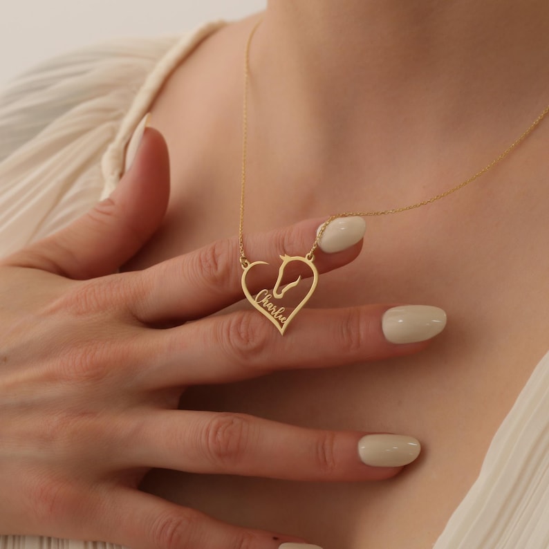 May include: Gold necklace with a heart-shaped pendant featuring a horse silhouette and the name "Charlie" inscribed inside.