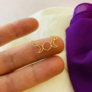 May include: A gold necklace featuring a triple moon pendant. The pendant is a simple design with three crescent moons and a circle in the centre.