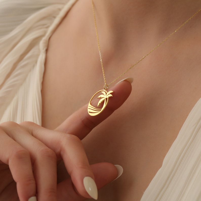 Puede incluir: Collar de oro con un colgante de palmera. El colgante es un dise&ntilde;o recortado de una palmera en una playa.