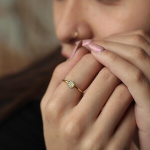 Puede incluir: Un anillo de oro con un peque&ntilde;o dise&ntilde;o de voleibol. El anillo tiene una banda delgada y un emblema circular de voleibol. El voleibol est&aacute; representado con detalles blancos y dorados. El anillo se lleva en un dedo.