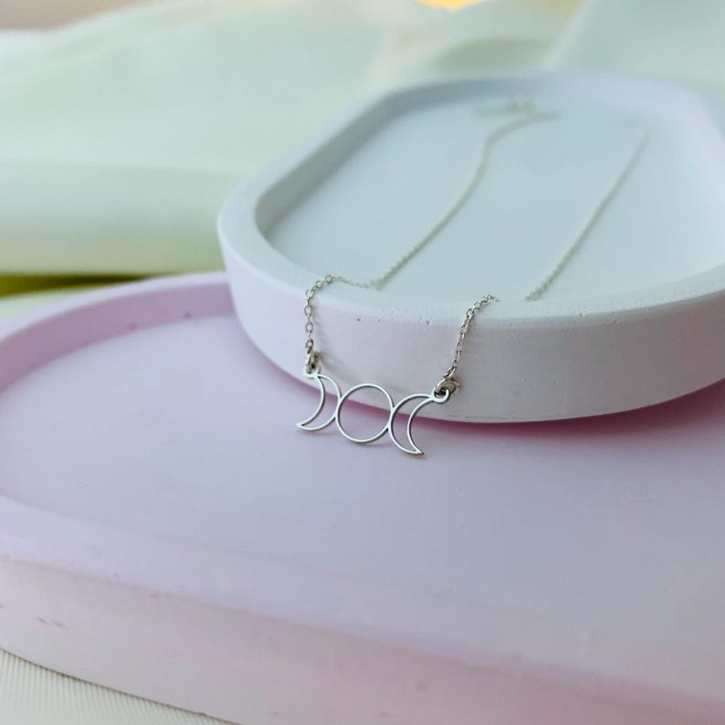 May include: A silver necklace featuring a triple moon pendant. The pendant is a simple outline of three crescent moons.