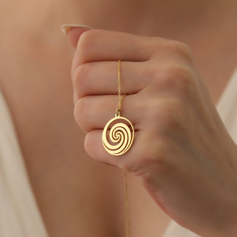 Puede incluir: Un collar de oro con un colgante circular con un dise&ntilde;o en espiral.