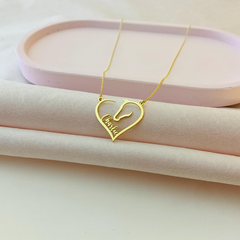 May include: Gold necklace with a heart-shaped pendant featuring a horse silhouette and the name "Charlie" inscribed inside.