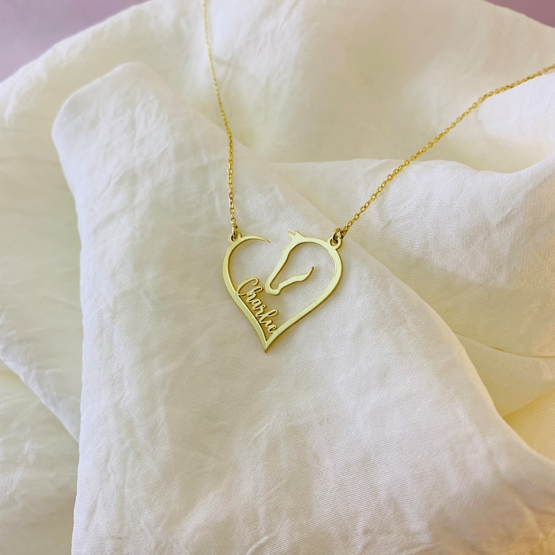 May include: Gold necklace with a heart-shaped pendant featuring a horse silhouette and the name "Charlie" inscribed inside.