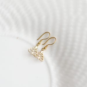 May include: A pair of gold-colored dangle earrings. Each earring features a delicate, openwork design with a star accent. The earrings have a hook closure and are displayed on a white surface.