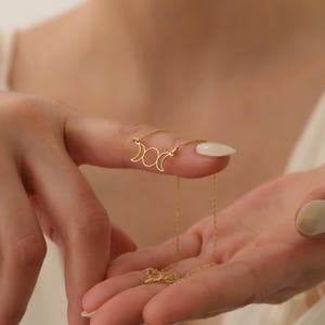 May include: A gold necklace featuring a triple moon pendant. The pendant is a simple design with three crescent moons.