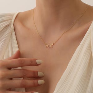 May include: A gold necklace featuring a triple moon pendant. The pendant is a delicate design of three crescent moons.