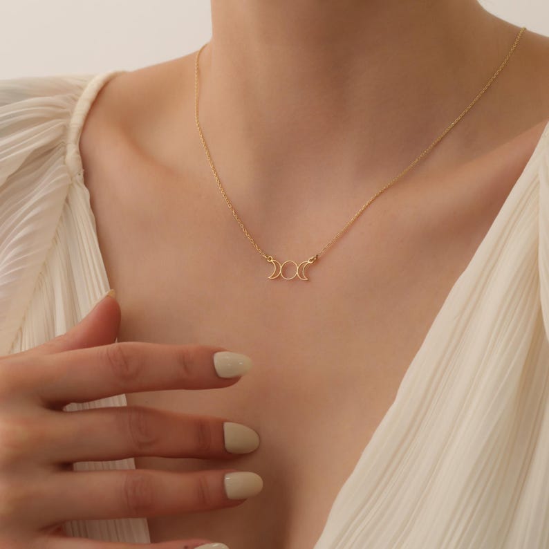 May include: A gold necklace featuring a triple moon pendant. The pendant is a delicate design of three crescent moons.