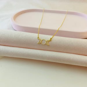 May include: A gold necklace featuring a triple moon pendant. The pendant is a delicate, open design with three crescent moons.