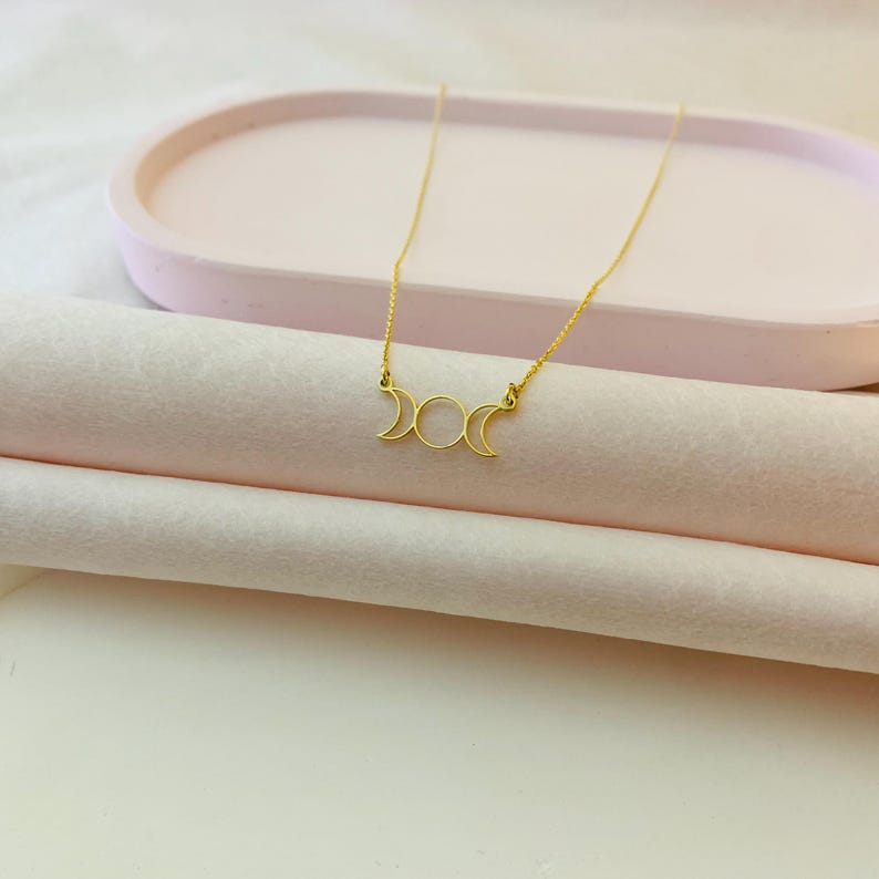 May include: A gold necklace featuring a triple moon pendant. The pendant is a delicate, open design with three crescent moons.