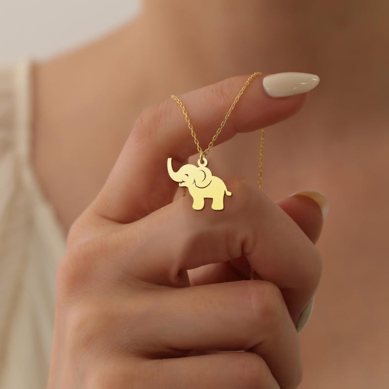 May include: A gold necklace with a small elephant pendant. The elephant is facing to the right and has a raised trunk.