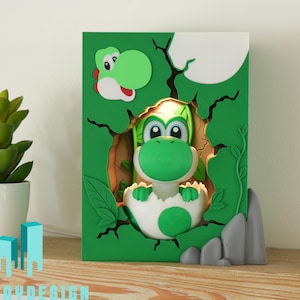 Könnte beinhalten: Ein grünes und weißes Yoshi-Nachtlicht. Das Licht zeigt ein 3D-Design von Yoshi, der aus einem Ei kommt, vor einem grünen Hintergrund mit einem Baum und einem Mond. Links ist eine kleine Sukkulentenpflanze in einem weißen Topf.
