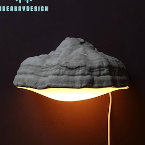 May include: A grey, mushroom-shaped wall lamp with a white cord. The lamp is lit and casting a warm glow.