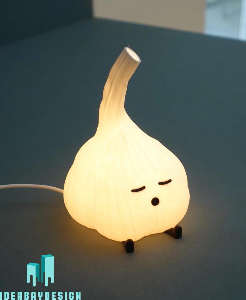 May include: A whimsical, glowing garlic-shaped lamp with a cartoon face, featuring closed eyes and a small mouth. The lamp emits a soft, warm light and has small black feet. The design is playful and unique, perfect for a bedroom or desk.