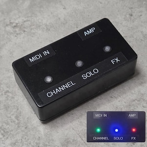May include: A rectangular black MIDI controller box featuring three circular indicator lights and labels for MIDI IN, AMP, CHANNEL, SOLO, and FX. An inset image shows the device with green, blue, and red LED lights illuminated on the top surface.