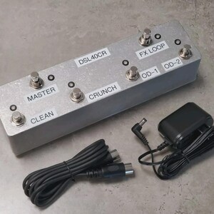 May include: A rectangular silver metal guitar amplifier footswitch with four metallic buttons and labels reading DSL40CR, FX LOOP, OD-1, OD-2, MASTER, CRUNCH, and CLEAN. It includes a black power adapter and a black multi-pin connection cable.
