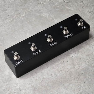 May include: A rectangular black guitar pedal switcher featuring five metallic footswitches arranged in a row. Each switch is labeled with white text reading CH-1, CH-2, CH-3, SOLO, and FX, accompanied by a small circular indicator light above each.