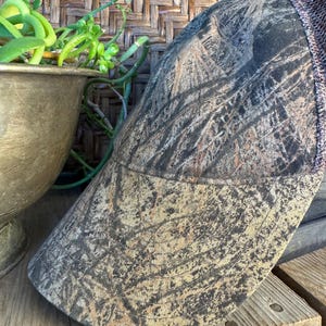 Puede incluir: Gorra de b&eacute;isbol de camuflaje con la parte trasera de malla marr&oacute;n y una visera curva. La gorra presenta un patr&oacute;n de color marr&oacute;n, beige y verde, que se asemeja a un dise&ntilde;o de bosque. El sombrero est&aacute; hecho de una tela duradera.