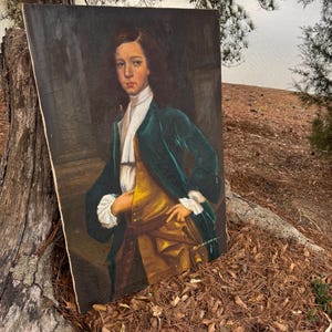 Pode incluir: Uma pintura de retrato antigo de uma pessoa jovem com um casaco de veludo verde, colete dourado e gravata branca. O retrato &eacute; contra um fundo escuro, com as m&atilde;os do sujeito na cintura. A pintura &eacute; exibida ao ar livre, encostada a um tronco de &aacute;rvore.