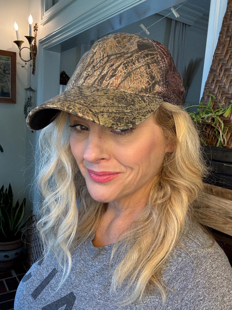 Puede incluir: Gorra de b&eacute;isbol de camuflaje con la parte trasera de malla marr&oacute;n y una visera curva. La gorra presenta un patr&oacute;n de marr&oacute;n, dorado y verde, creando un dise&ntilde;o de camuflaje de bosque. El sombrero es de estilo cl&aacute;sico de seis paneles.