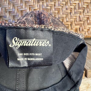 Puede incluir: Gorra de b&eacute;isbol negra con una parte superior de malla estampada y una visera negra. La etiqueta dice "Signatures" y "Talla &uacute;nica". Hecho en Bangladesh.