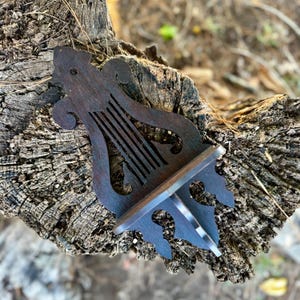 May include: A dark brown, wooden decorative shelf with a lyre-shaped design. The shelf has a small, rectangular surface for displaying items and is supported by a decorative bracket. The shelf is placed on a weathered tree stump.