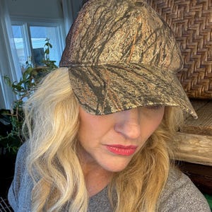 Puede incluir: Gorra de b&eacute;isbol de camuflaje con un patr&oacute;n marr&oacute;n y verde. La gorra tiene una parte trasera de malla y una visera curva. El sombrero est&aacute; dise&ntilde;ado para actividades al aire libre y proporciona protecci&oacute;n solar.