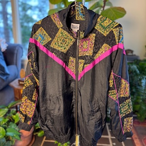 Puede incluir: Chaqueta deportiva vintage negra con cremallera completa, con patrones geométricos en amarillo, verde y azul. La chaqueta tiene detalles en rosa brillante y el texto "BASIC COTTON" en la etiqueta.