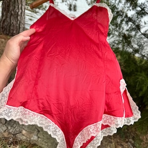 May include: A red satin slip with white lace trim. The slip has thin straps and a V-neckline.