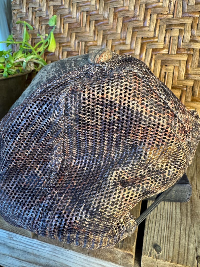 Puede incluir: Gorra de estilo newsboy de malla marr&oacute;n, negra y beige. La gorra tiene una corona redondeada y una visera corta y r&iacute;gida. El dise&ntilde;o de malla proporciona ventilaci&oacute;n. La gorra est&aacute; colocada sobre una superficie de madera.