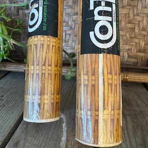 May include: Two rolls of Contact brand self-adhesive plastic with a wood grain pattern. The rolls are wrapped in clear plastic and have black and white labels. The wood grain pattern is a mix of light and dark brown.