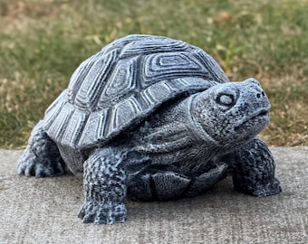 May include: A detailed, gray concrete turtle statue with a textured shell and realistic features. The sculpture is positioned on a concrete surface, showcasing its intricate design and outdoor garden decor theme.