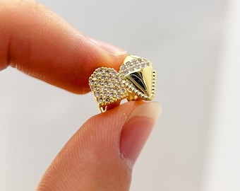May include: A pair of gold-colored stud earrings. One earring is heart-shaped and covered in small, clear crystals. The other earring is a pyramid shape with a pointed tip and also features clear crystals.