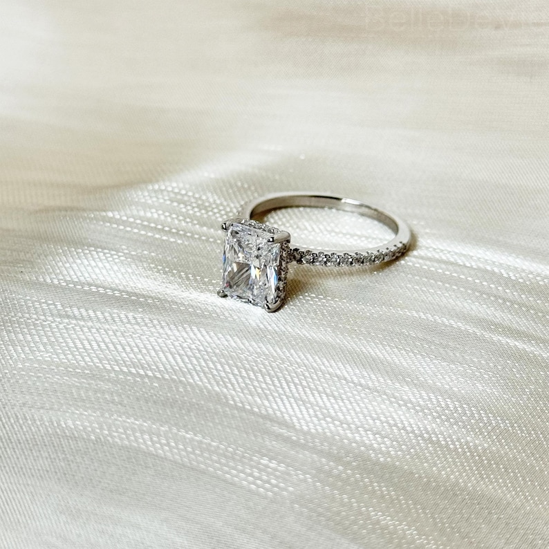 May include: A silver ring with a large, square-shaped diamond and a band of smaller diamonds.