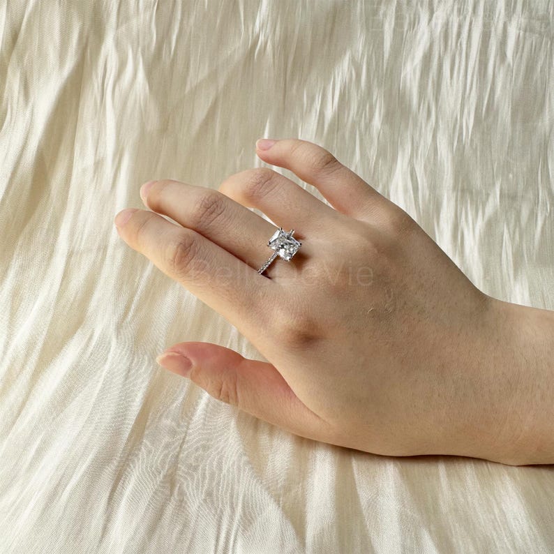 May include: A silver ring with a large, square-shaped, clear cubic zirconia stone. The ring has a pave setting with smaller cubic zirconia stones around the main stone.
