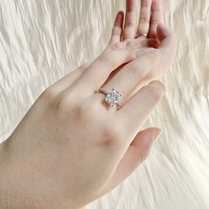 May include: A silver ring with a large, clear, square-shaped gemstone. The ring is set with smaller diamonds around the gemstone.