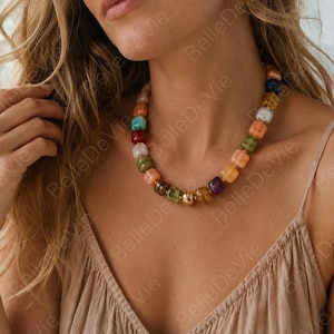 May include: A necklace featuring a series of multi-colored, square-shaped beads in shades of red, orange, yellow, green, blue, and purple, interspersed with small gold-toned spacers and a single central gold-toned spherical bead.