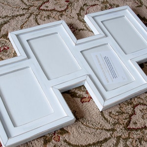 May include: A white multi-photo frame with a unique zig-zag design. The frame has five rectangular openings for photos and a distressed finish. The frame is made of wood and is suitable for displaying multiple images.